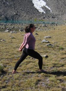 person in warrior I yoga pose with hands clasped behind them